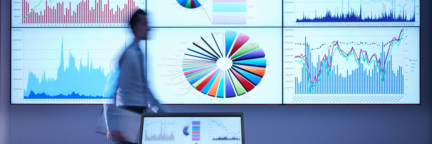 A man in front of a large screen with data and charts on it.