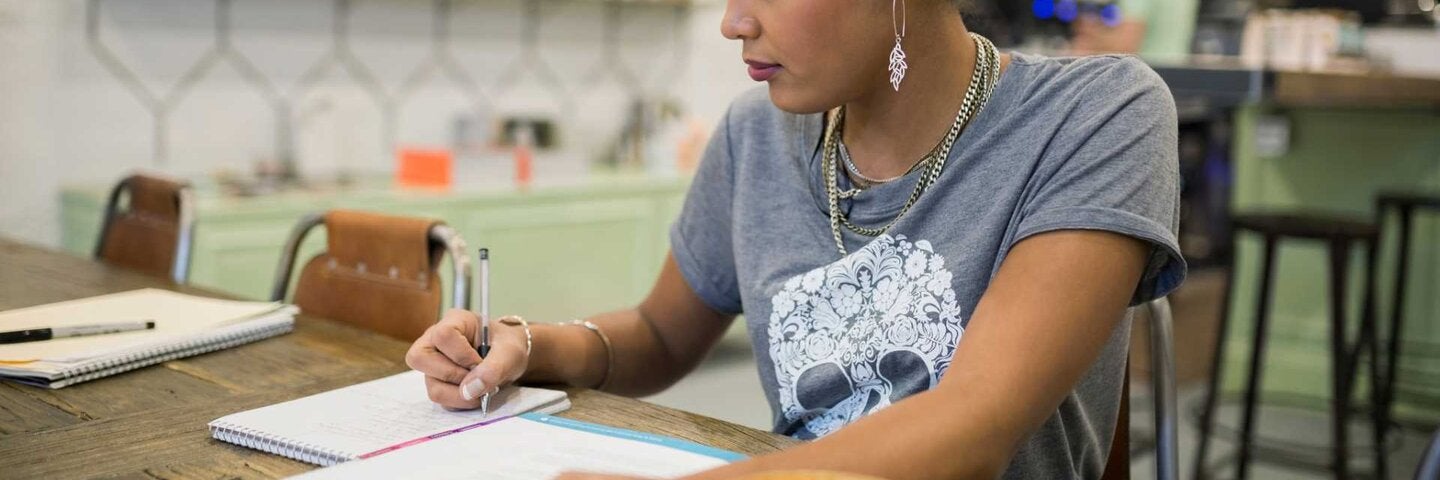 woman sitting at a table in a coffee shop, writing in a notebook
