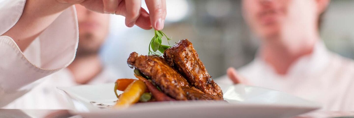 close up of chef's hand putting garnish on a plate