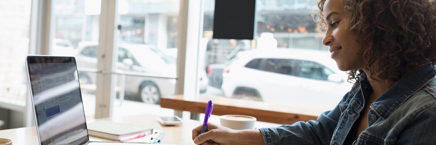 Smiling woman working at laptop, taking notes in cafe