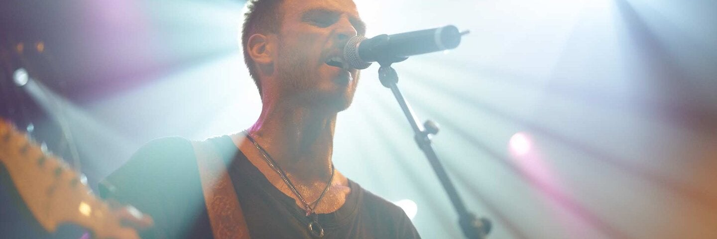 A young man singing and playing guitar on the stage at a music festival. 