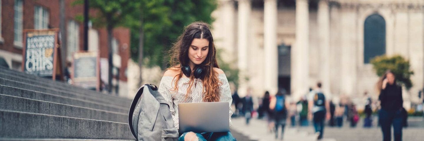 Woman in UK typing on laptop while sitting on steps.