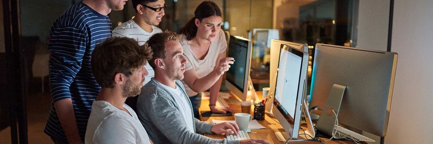 Shot of a group of young people using a computer together during a late night in a modern office