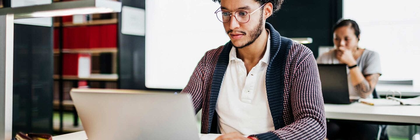 Young Man Working On Laptop While Studying In Library