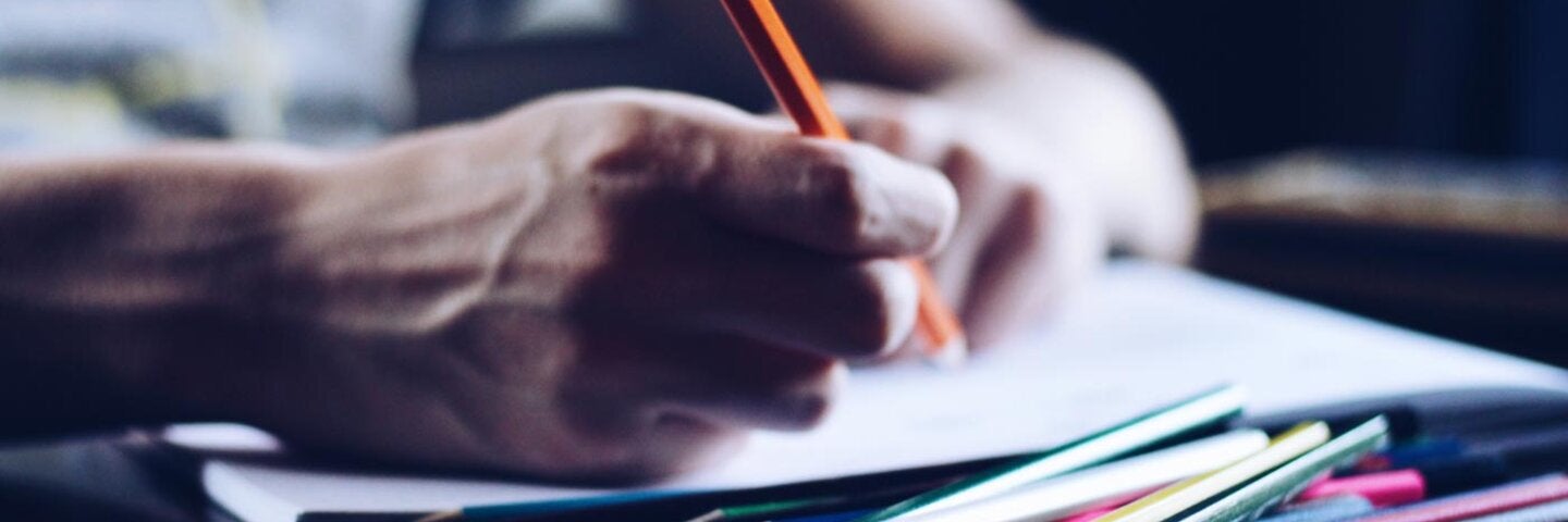 hands writing with a pencil on a stack of papers