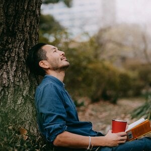 man sitting beneath a tree with coffee and 
